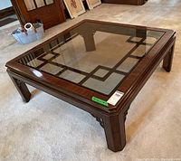 Front-side angled view of wood coffee table with glass top showing polished dark wood and geometric accents.