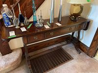 Front and top view of the console table showing three drawers, metal drawer pulls, and dark wood finish with some wear. Various objects on top not included in sale.