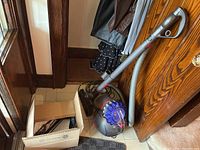 Full view of Dyson Big Ball Extra canister vacuum with gray hose, handle, and motorized floor head alongside a cardboard box containing additional small attachments.