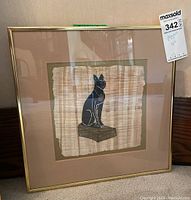 Framed artwork showing full view of the Egyptian cat papyrus piece in a gold-tone metal frame with a beige matte.