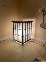 Lighted end table illuminated in a corner showing glowing light through white panels with black grid.
