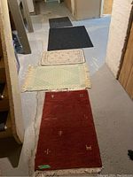 Five rugs laid out on a basement floor showing variety in sizes, colors, and styles.