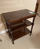 Side view of the wooden side table showing two lower shelves and turned spindle legs.
