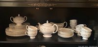 Wide shot showing most of the china pieces on a shelf, including stacked plates, teapot, sugar bowl, creamer, cups, and saucers.