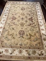 Full view of beige floral patterned area rug showing overall design and wear