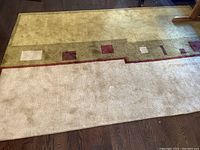 Photo of the area rug showing green, beige, and burgundy sections with slight wear and stains.