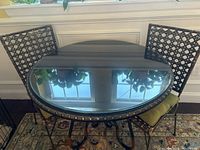 Full view of round bistro table with glass top and two chairs on sides.