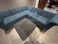 Front view of blue sectional sofa composed of five connected sections with tufted back cushions. Large gray ottoman positioned in front of sofa.