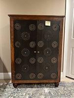 Closed view of a wooden cabinet with two black metal doors featuring circular stud patterns.
