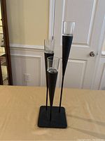 Front view of black metal candle holder with three glass candle containers on a square base