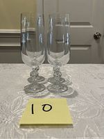 Two clear crystal champagne glasses shown standing on a lace tablecloth with a door in the background. The glasses are slender with decorative stems.