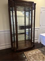 Front-facing view of tall wooden china cabinet showing glass doors and shelves along with carved decorative wooden accents on top and sides.