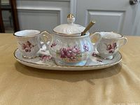 Front view of porcelain espresso set with two cups, sugar bowl with lid and spoon on platter showing floral pattern and gold trim details