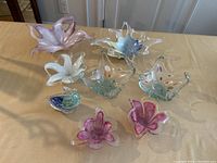 Collection of eight Murano glass figurines and bowls arranged on a table showing the varied shapes and colors.