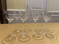 Photo of 8 clear long stem wine glasses arranged on a table, showing front and side views to display shape and condition.