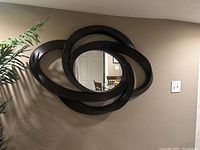 Front view of large dark wood decorative wall mirror mounted on a beige wall, showing the oval overlapping frame design