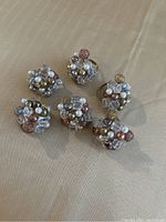 Set of six gold and white decorative napkin rings arranged on a solid surface showing cluster bead embellishments and gold bands.