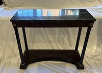 Sofa table viewed from angled top side, showing polished black marble top and dark wood frame with brass accent