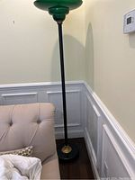 Full view of the tall standing lamp next to a beige sofa, showing green glass lighting fixture and black pole.