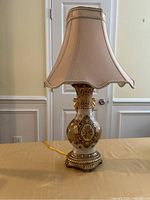 Front view of the old fashioned table lamp showing the porcelain base with intricate patterns and scalloped fabric shade.