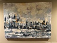 Abstract cityscape painting on canvas with blue, grey, and yellow tones against a wall.