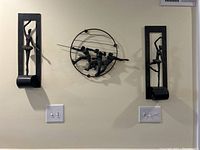 Full view of the three metal wall art pieces installed on a wall showing swordsmen and ballerinas