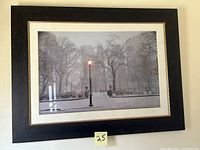 Framed black and white cityscape of Philadelphia with trees, streetlamp, park fencing, and misty buildings.