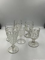 Front view of six antique pressed glass goblets with various cut glass patterns