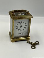 Front view of brass French carriage clock with winding key placed foreground