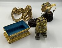 Group photo of five Asian decorative items including a cloisonné dragon, cloisonné bird on black base, cloisonné foo dog, and two rectangular enamel trinket boxes with blue interior and gold-tone base.