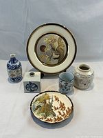 Full lot of six Asian pottery pieces displayed on neutral fabric, showing all items including the limited edition plate, various vases, cup and plates.