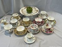 Overall view of nine teacup and saucer sets, creamer, sugar bowl and cake stand arranged on table