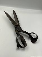 Photo of large antique tailor scissors showing the full open blades and ergonomic handles with patina on metal.