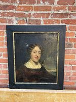 Full frontal view of the framed oil painting against a brick background.