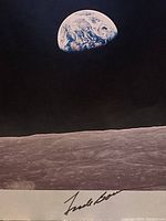 Earth rising above lunar surface with signature at bottom border