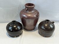 Three Asian pottery pieces grouped together on white background - large brown vase and two smaller dark brown soy sauce jugs