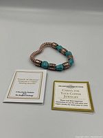 Photo of the bracelet arranged in a heart shape alongside two cards, one with the Touch of Heaven branding and the other with copper care instructions.