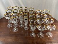 Front view of 28 gold-rimmed crystal glasses arranged in rows on a wooden table