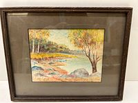 Full framed watercolour landscape painting showing autumn trees, rocks, water, and signature in the lower right corner.