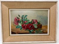 Framed still life oil painting showing red and pink roses with green leaves on a wooden surface.