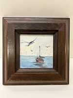 Full view of the framed oil painting depicting a boat in the water with seagulls flying above.