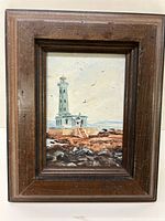 Full view of the framed oil on board painting showing a lighthouse on a rocky shore with birds in the sky.
