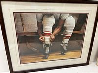 Photo showing framed hockey art of player lacing skates from a frontal angle.