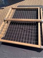 Full view of dog gate showing wooden frame with black metal wire grid laying on a black cloth surface outdoors.