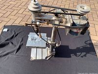 Full view of older bench drill press showing entire unit with pulley system, three-lever feed handle, and base plate with some included hardware.
