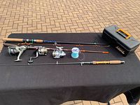 Overview of three fishing rods, three reels, fishing line spool, and black plastic gear box with orange handle