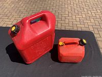 Two red gasoline fuel containers of different sizes on a black surface outdoors.