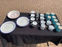 Photo of ceramic mugs and plates on a black cloth table, includes Royal Winton Pottery mugs and several other ceramic mugs and plates