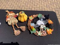 Photo showing the scarecrow doll, yellow gourd, and Halloween wreath arranged on a black surface outdoors.