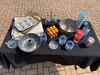 Full overview of all housewares arranged on black cloth outdoors on brick surface, showing baking dishes, juice press, mugs, bottles, and other items.